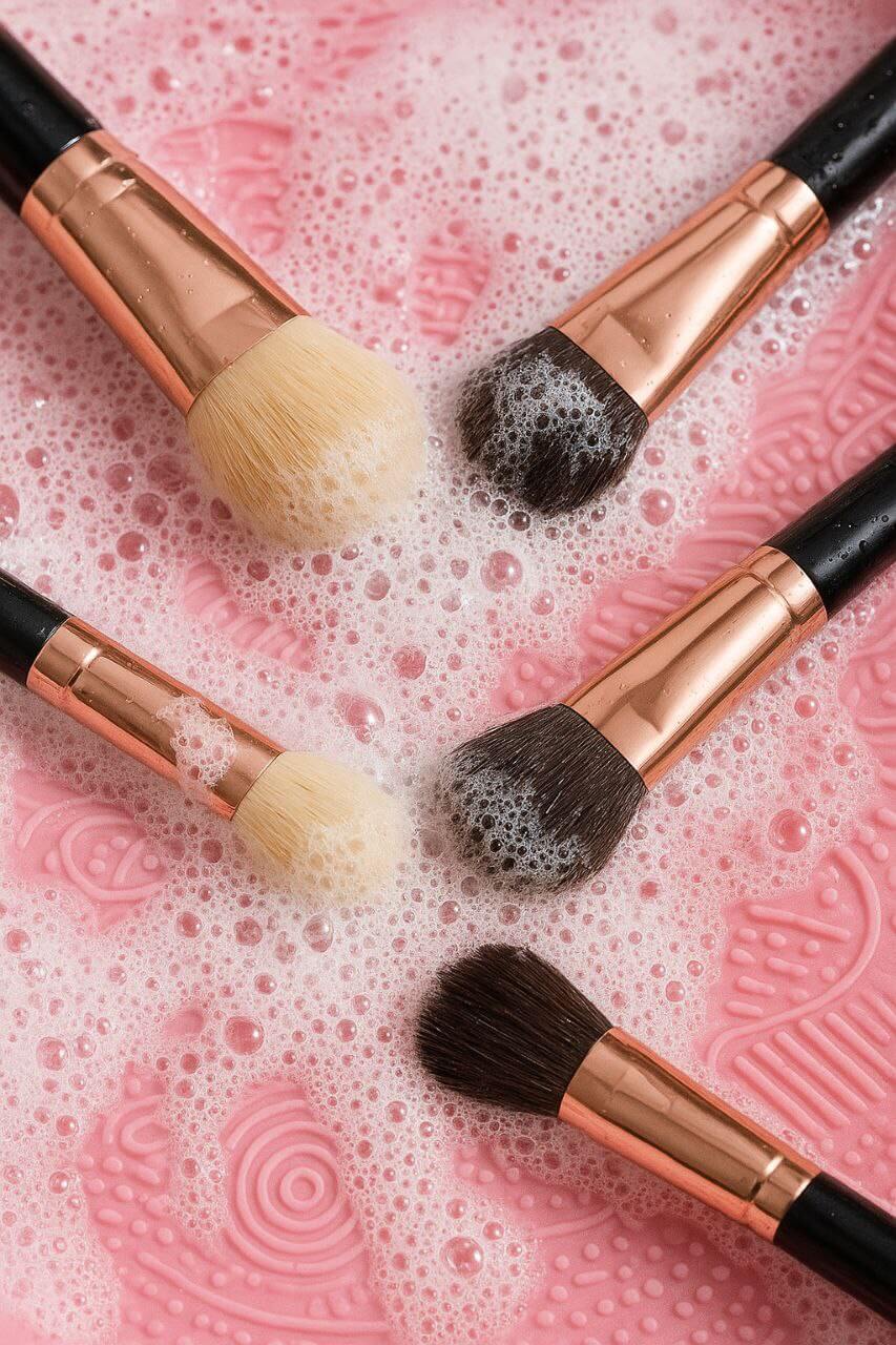 "Makeup brushes being cleaned in soapy water with silicone cleaning mat"